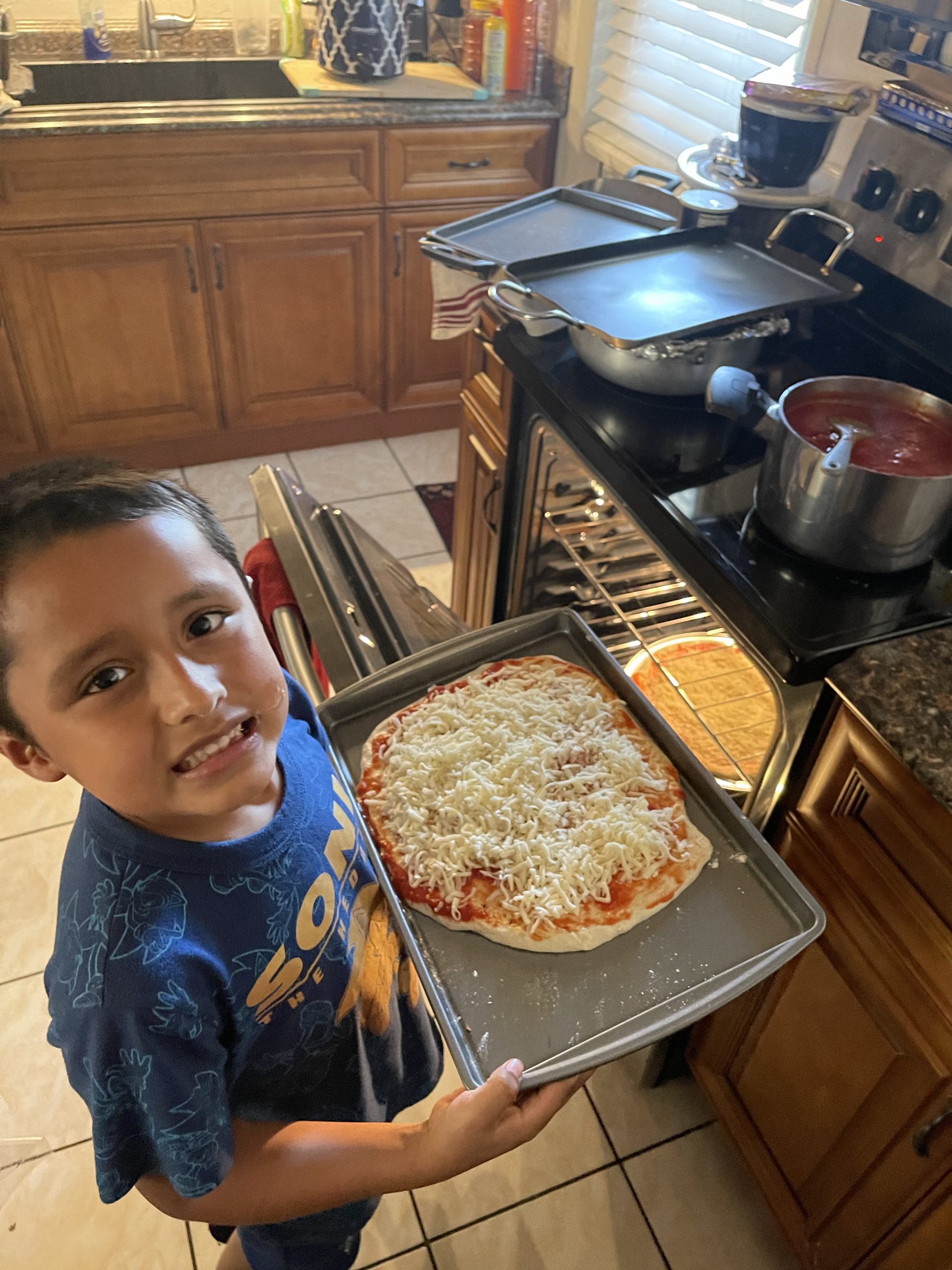 A young boy holding up a pan of pizza.