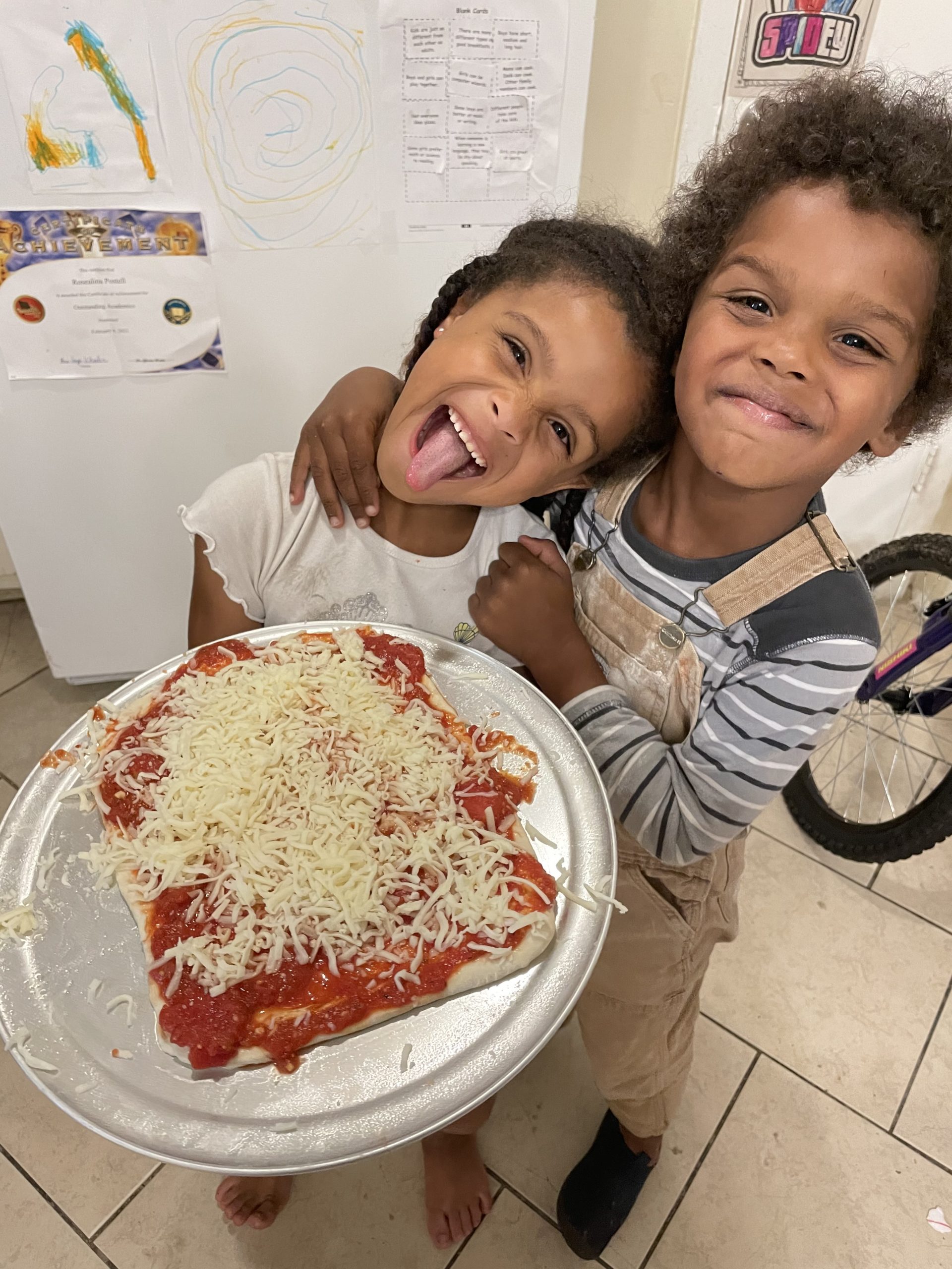 Two children are holding a pizza on the floor.